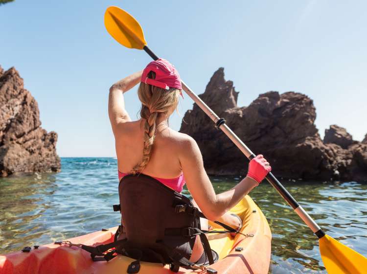 Horizontal color image of woman kayaking in Mediterranean sea. Beautiful woman rowing with oar. Exploration of Mediterranean seascape.
