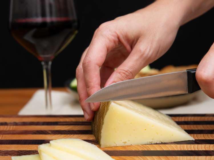 Female hands cutting hard cheese on wooden board. Traditional appetizer. Studio shot. Selective focus. Side view. Dairy food and cooking at home concept for flyers and banners