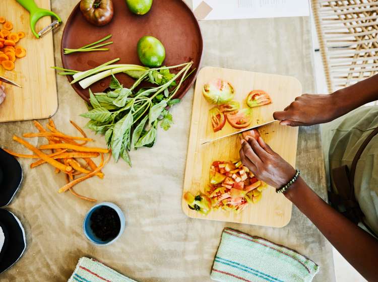 Medium overhead shot of woman slicing organic heirloom tomatoes while taking vegetarian cooking class in demonstration kitchen