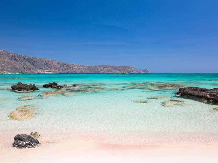 View across the clear turquoise waters of Vroulia Bay from sandy beach, Elafonisi Islet, Elafonisi (also known as Elafonissi), Hania (also known as Chania), Crete, Greece, Europe. Famous for its stunning beaches of fine pink sand, Elafonisi lies on the Libyan Sea at the southwestern tip of the island.