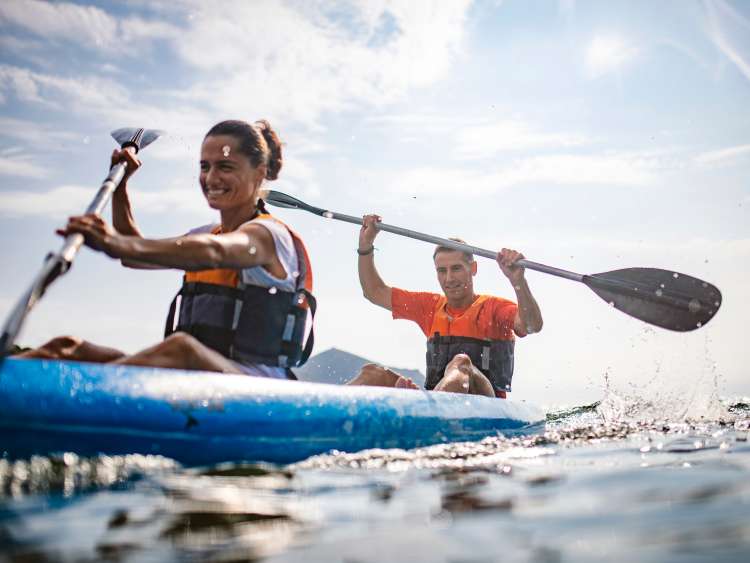 Water surface level view of energetic male and female kayakers in 30s and 40s paddling past camera in Mediterranean Sea off the Costa Brava.