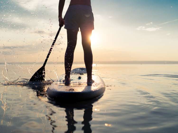 summer sunset SUP rear view part of woman paddling with stand up paddle board alone in lake