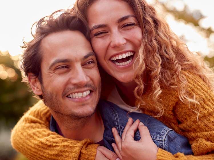 Portrait Of Happy Loving Couple With Man Giving Woman Piggyback As They Hug In Autumn Park Together