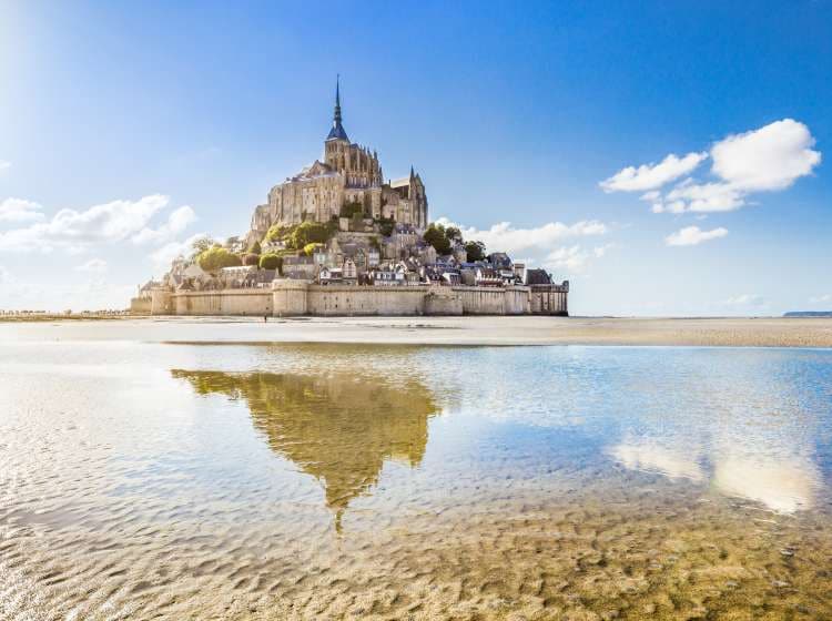 Panoramic view of famous Le Mont Saint-Michel tidal island on a sunny day with blue sky and clouds, Normandy, northern France.
