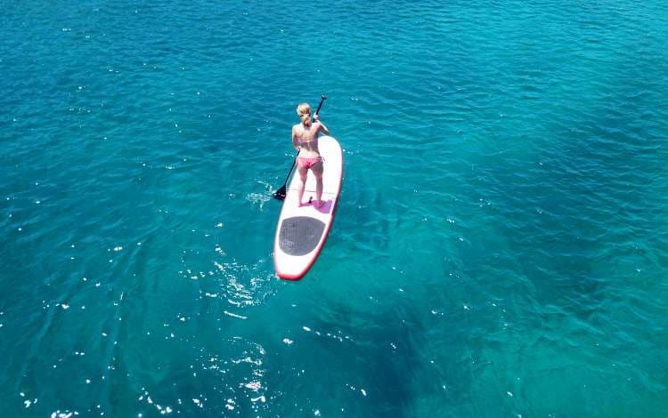 Aerial drone bird's eye view photo of attractive young woman practicing paddle board or sup in tropical caribbean sapphire crystal clear calm waters; Shutterstock ID 1121881937; Invoice Number: -