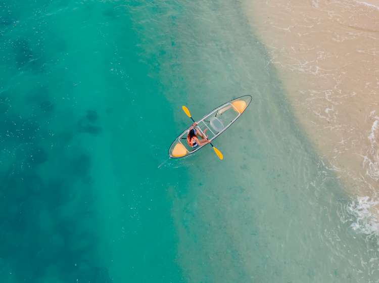 aerial view of blue sea with floating transparent kayak is going into sand beach, person with life jacket on boat