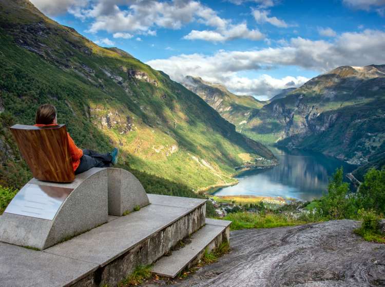 Tourism vacation and travel. Female tourist enjoying view over Geirangerfjord from Flydalsjuvet viewpoint seat, Norway. Tourist attraction.