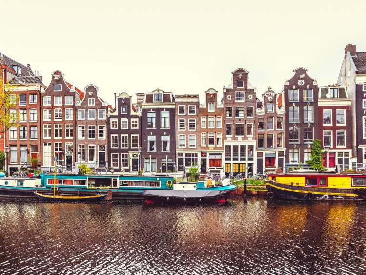 Dancing house in Amsterdam Netherlands over river Amstel panorama of traditional Dutch architecture with boat on bank urban landscape.; Shutterstock ID 652553899; Invoice Number: -