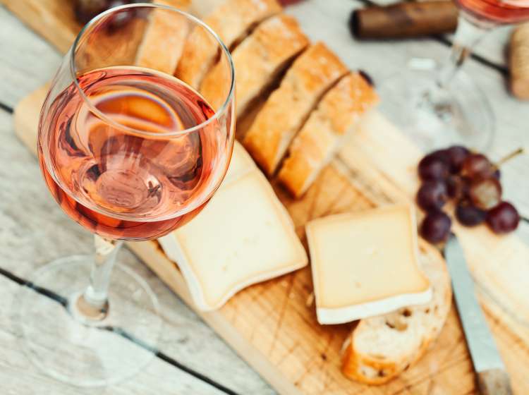 Two glasses of rose wine and board with fruits, bread and cheese on wooden table