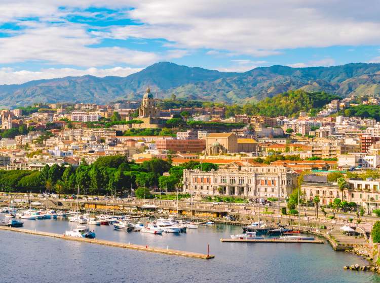 Cityscape of Messina, Sicily, Italy. Multi colored image with buildings, cathedral, mountains, blue sky with clouds, boats and yachts in the harbor or cruise port of Messina.