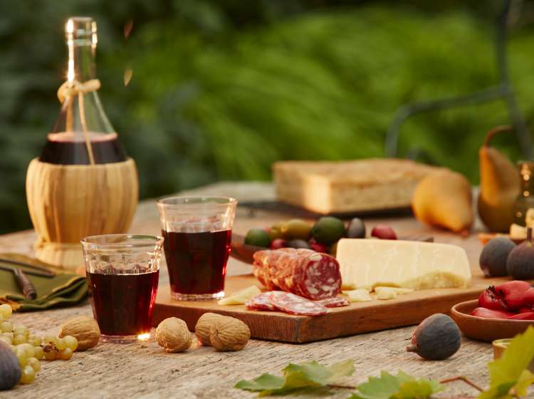 red wine with salami, cheeses, olives, figs and peppers in out door picnic setting