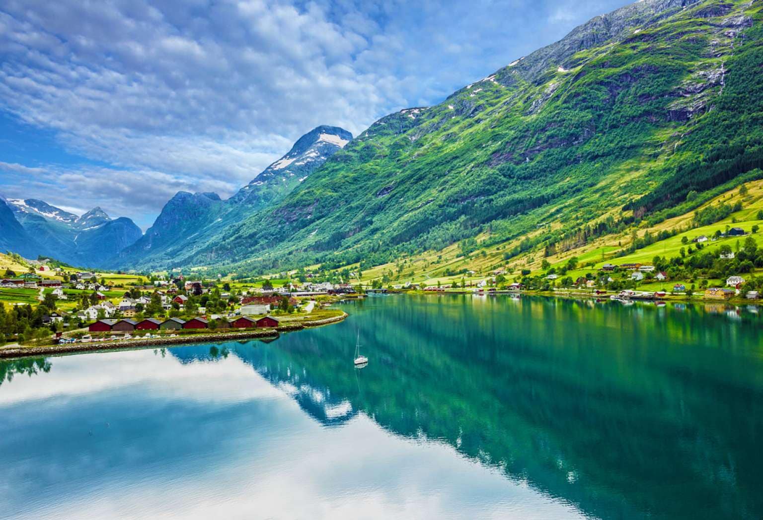 Big green mountains next to water and houses 