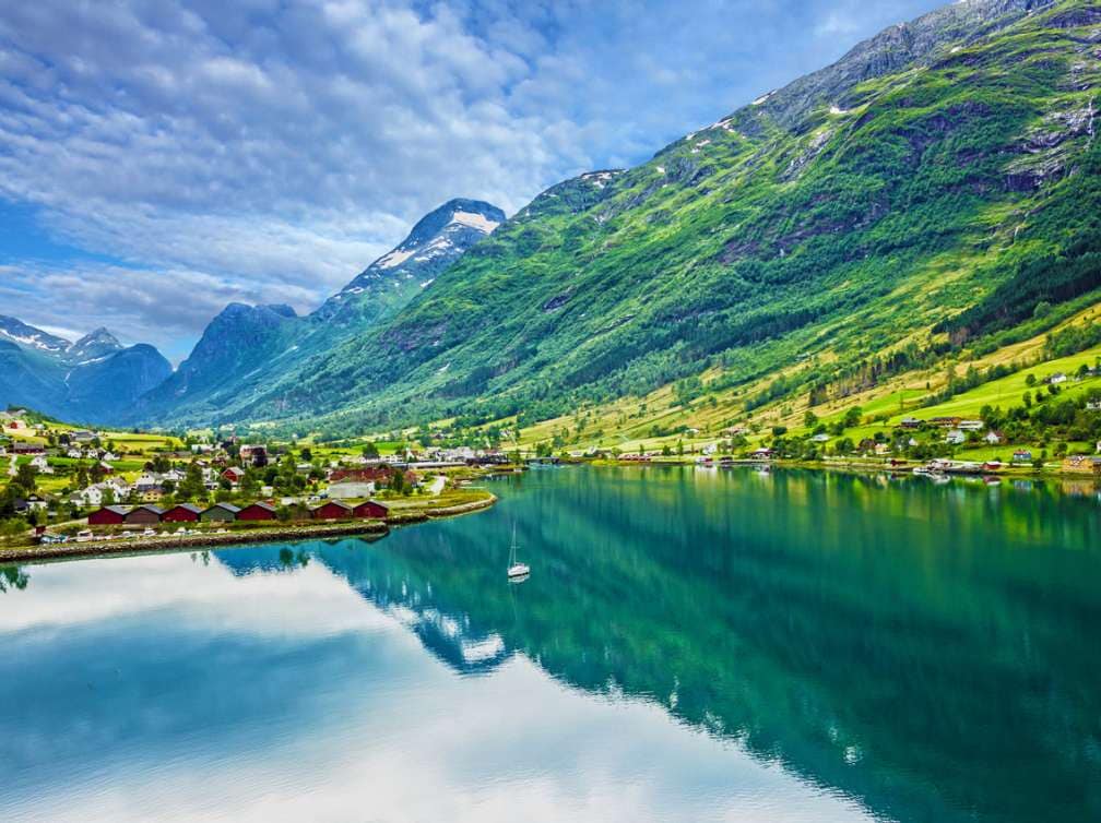  Big green mountains next to water and houses 