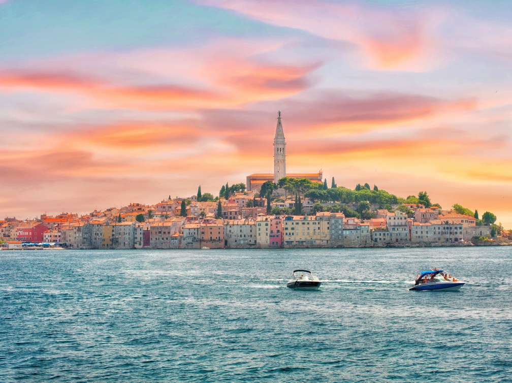 Two speedboats in sea in front of town lit up by sunset