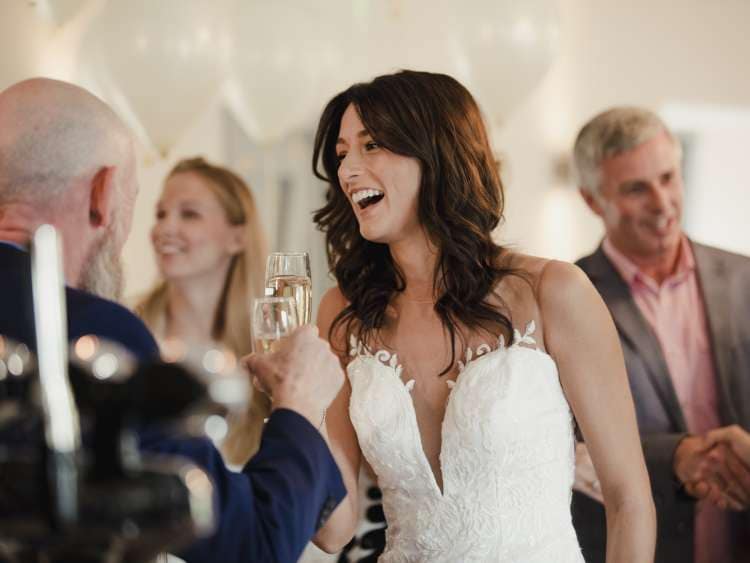 Beautiful bride is socialising with her father and family on her wedding day. They are drinking champagne and laughing together.