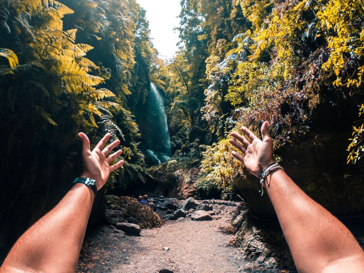a person with their hands out towards a waterfall in La Palma
