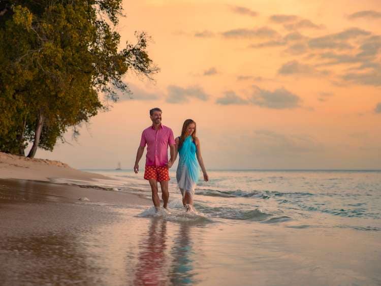 Couple walking along a beach in Barbados with the tide coming in