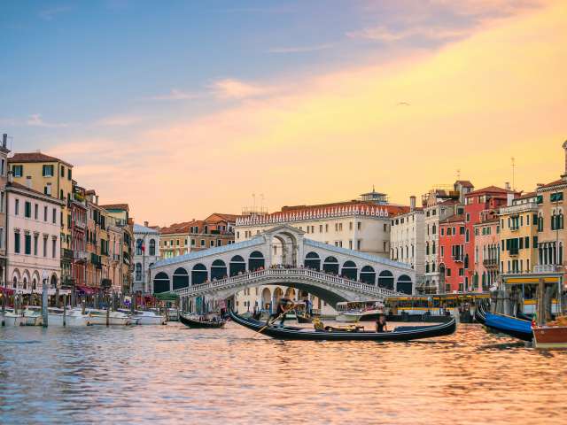  Gondaliers rowing past the Rialoto Bridge in Venice, Italy, at sunset