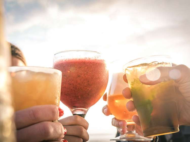 Greetings to best friends, group of friends enjoying evening drinks at the beach at sunset. Concept of vacation, carefree, end-of-day relaxation, celebration and well-being.