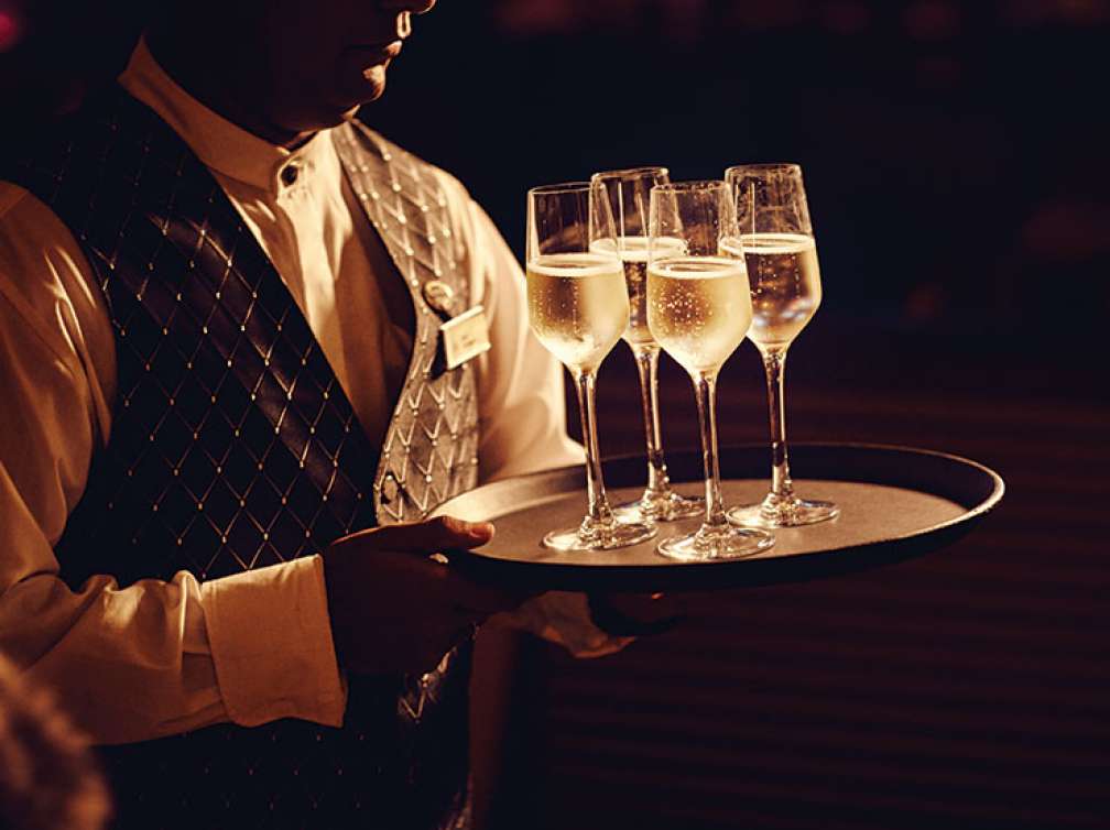 Waiter holding 4 champagne glasses on tray 