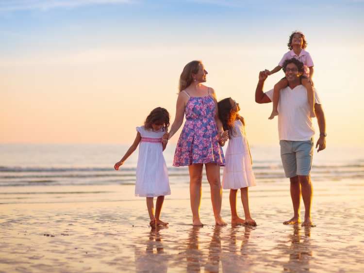 Family with kids walking on tropical beach at sunset. Cute little kids running with parents. Travel with kid. Summer vacation on sea shore. Family holiday with children. Water sport fun.