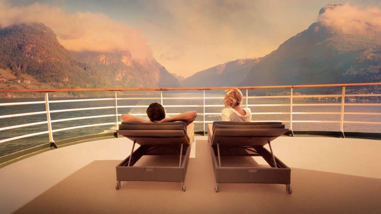 Two people on the front of a cruise ship infront of mountains