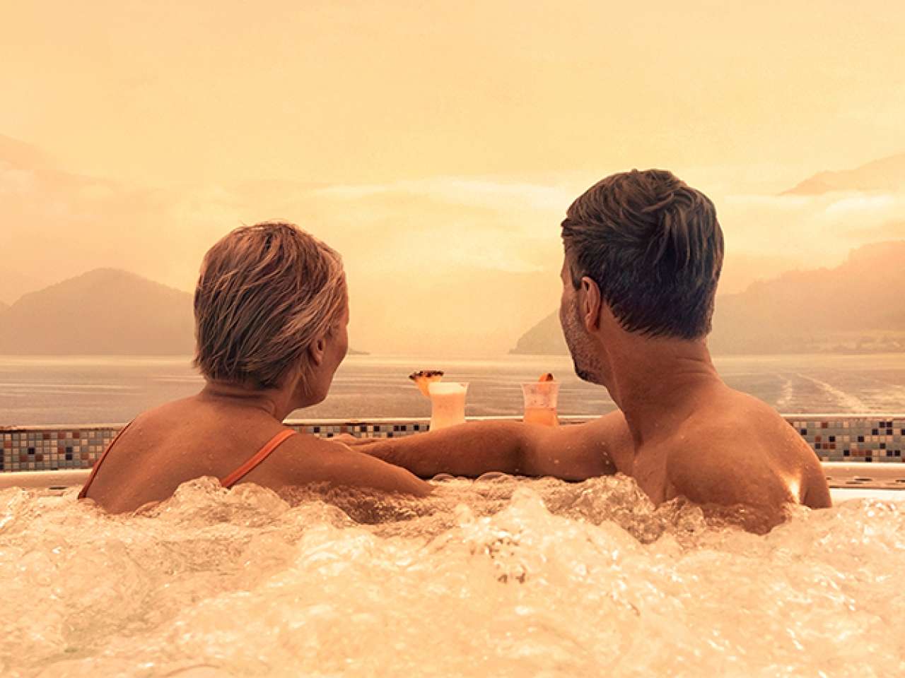 Couple enjoying drinks in a whirlpool spa watching the wake of the ship