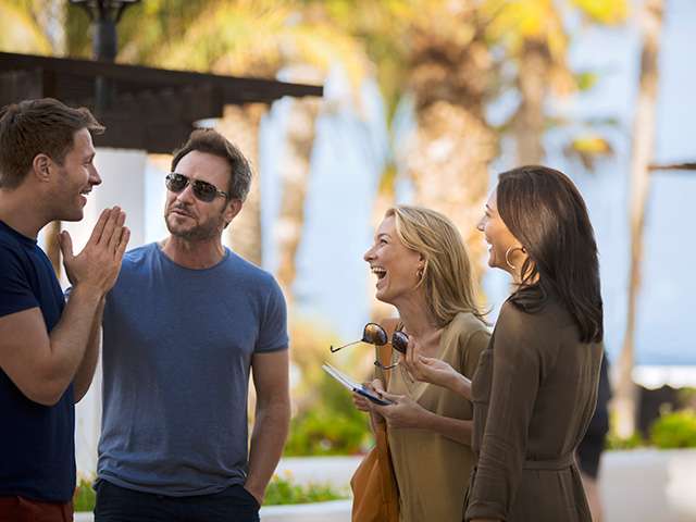 Friends laughing together near palm trees on beach 