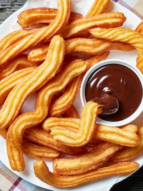 close-up of churros - Traditional Spanish and mexican dessert on a white plate with chocolate sauce on an old grey rustic wooden table, horizontal view from above