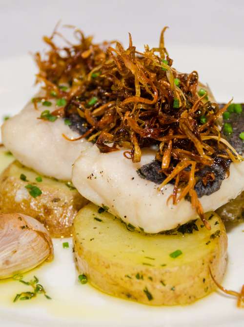Hake fillet topped with crispy onion on a potato layer in garlic style