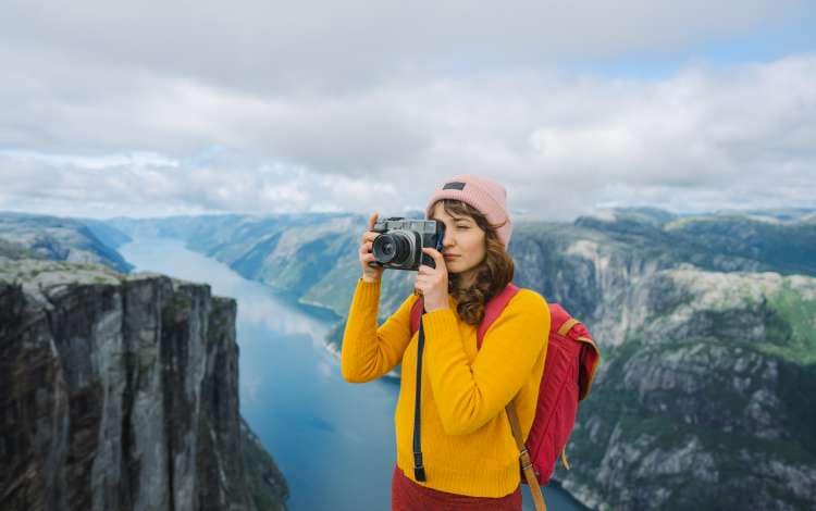 Woman  in yellow and red outfit photographing  Lysefjorden from Kjerag mountain