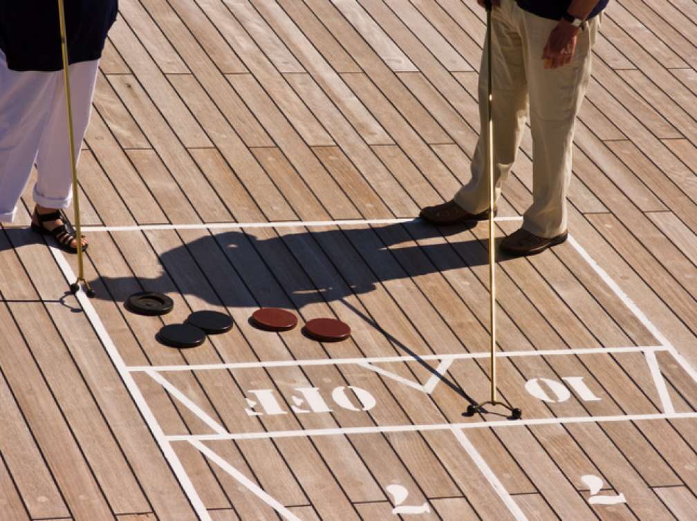 A man and a woman playing shuffleboard on the deck of the Queen Mary 2.