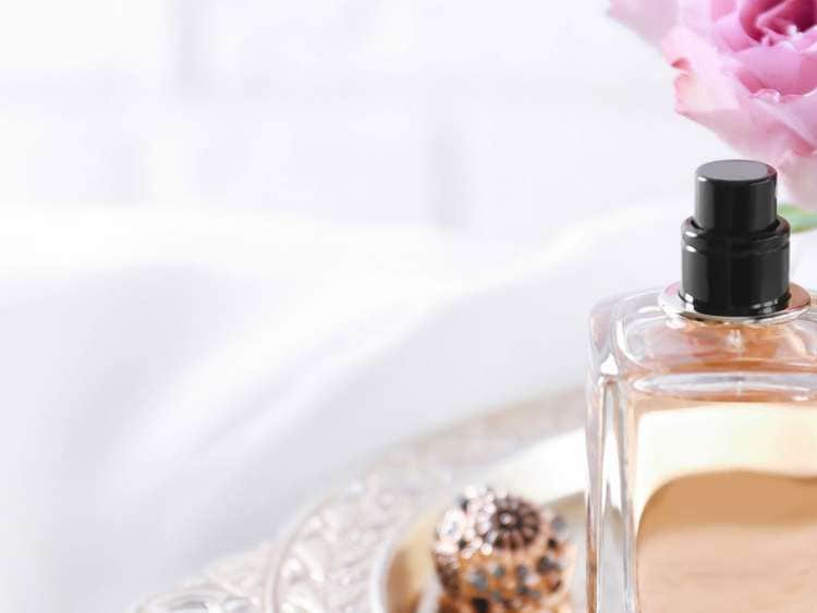 Metal tray with bottle of perfume and flowers on light background