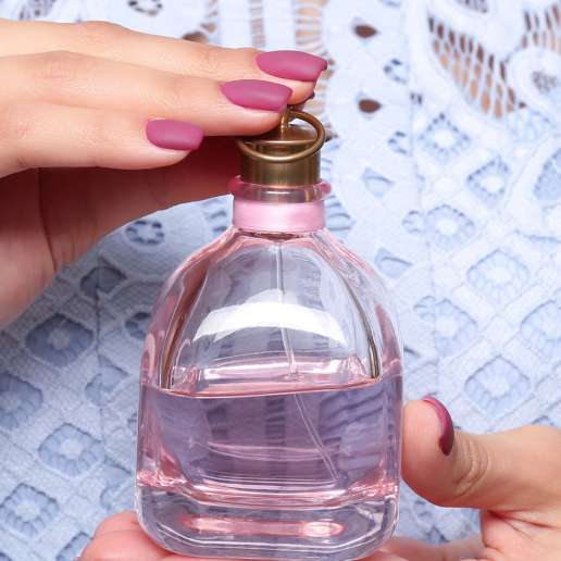 Beautiful young woman with bottle of perfume on light background, closeup