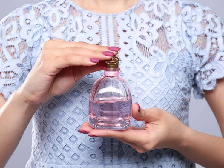 Beautiful young woman with bottle of perfume on light background, closeup