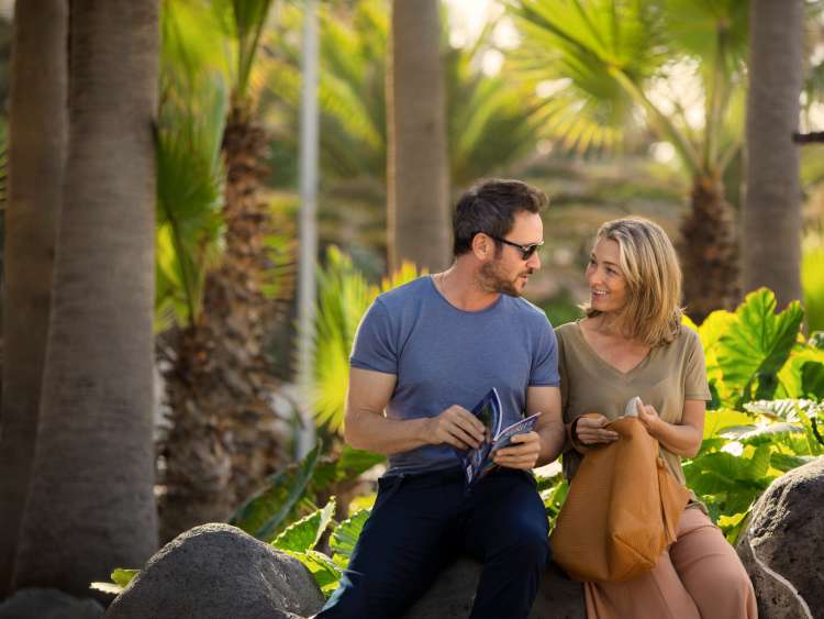 Couple sat together in gardens talking and reading travel guide