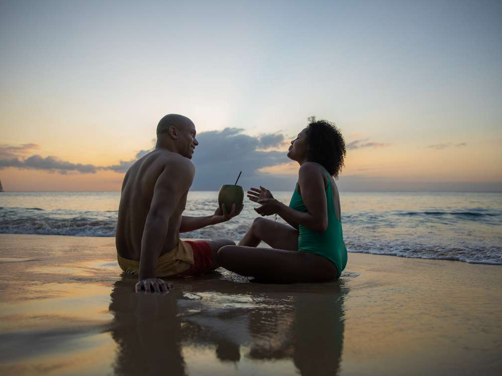 Couple enjoying a drink sitting on the beach at dusk with the tide coming in