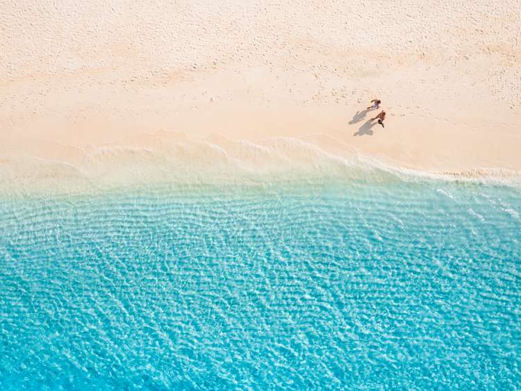 Aerial view of amazing beach with couple walking in sunset light close to turquoise sea. Top view of summer beach landscape, romantic love couple vacation, romantic holiday. Freedom leisure activity