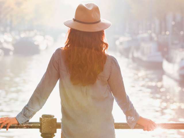 Lady with hat looking into river from bridge in Amsterdam