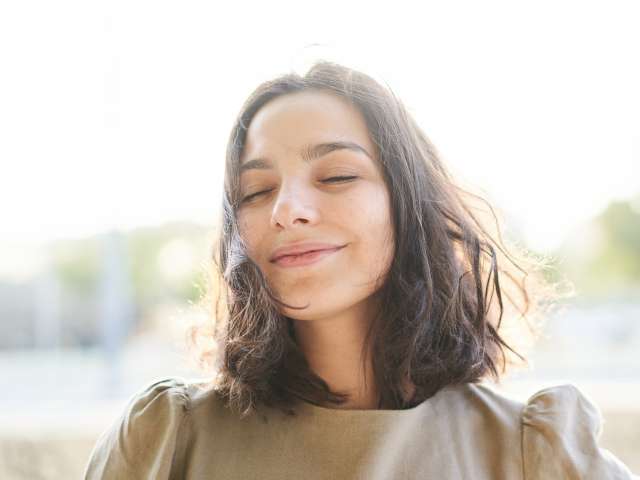 Close-up of a beautiful caucasian young woman standing front of the camera with eyes closed and satisfied face while the wind blows her hair