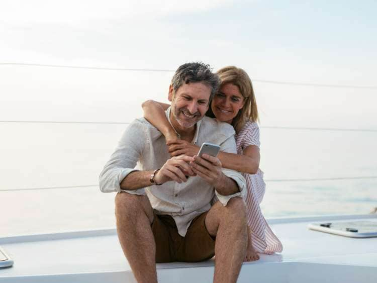 Mature couple looking at smartphone, sitting on a sailing boat