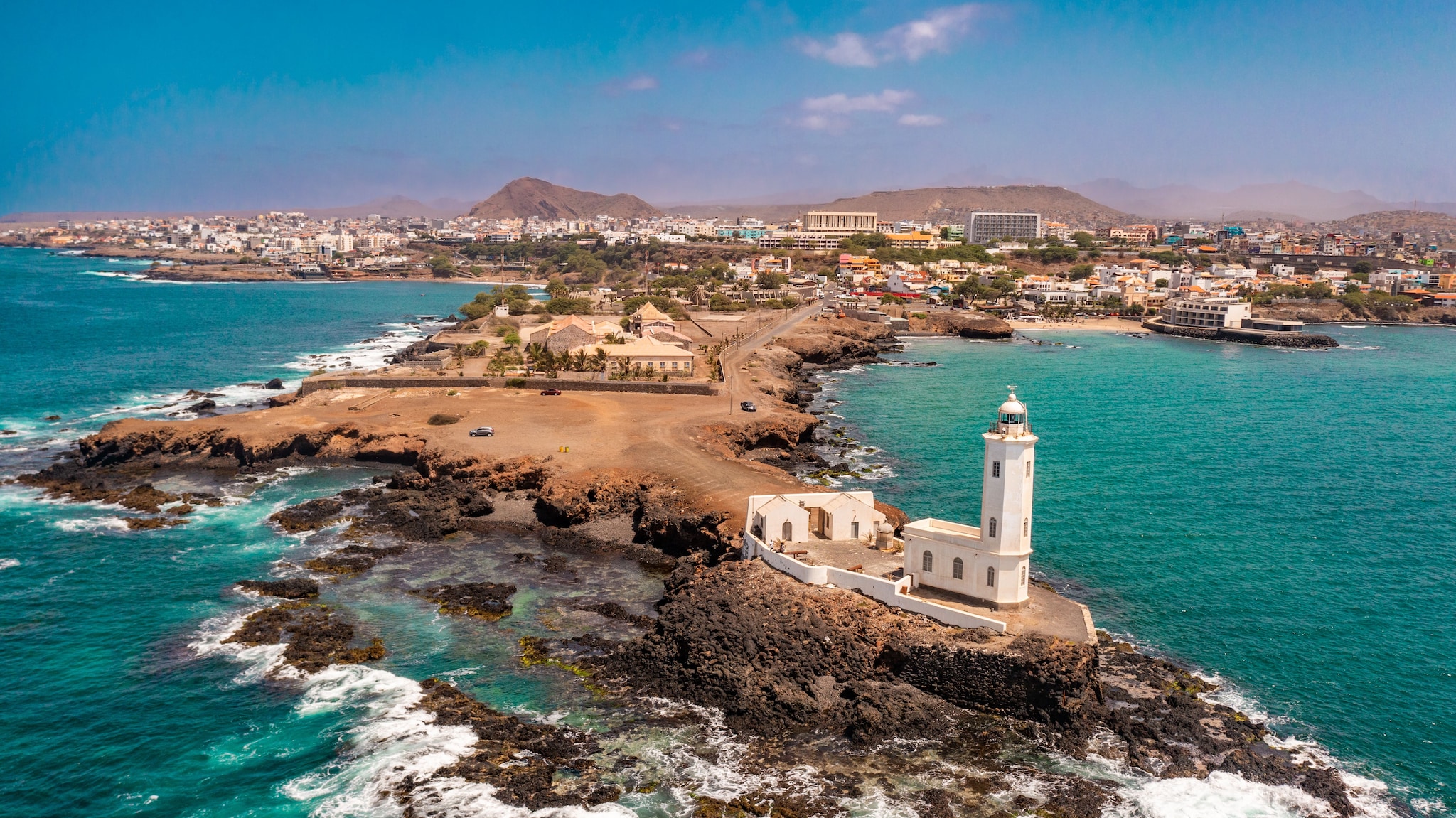 {"metadata_en_GB":{"alt-text":"An aerial view of the shore of Praia de Santiago and the Praia lighthouse on a sunny day"}}