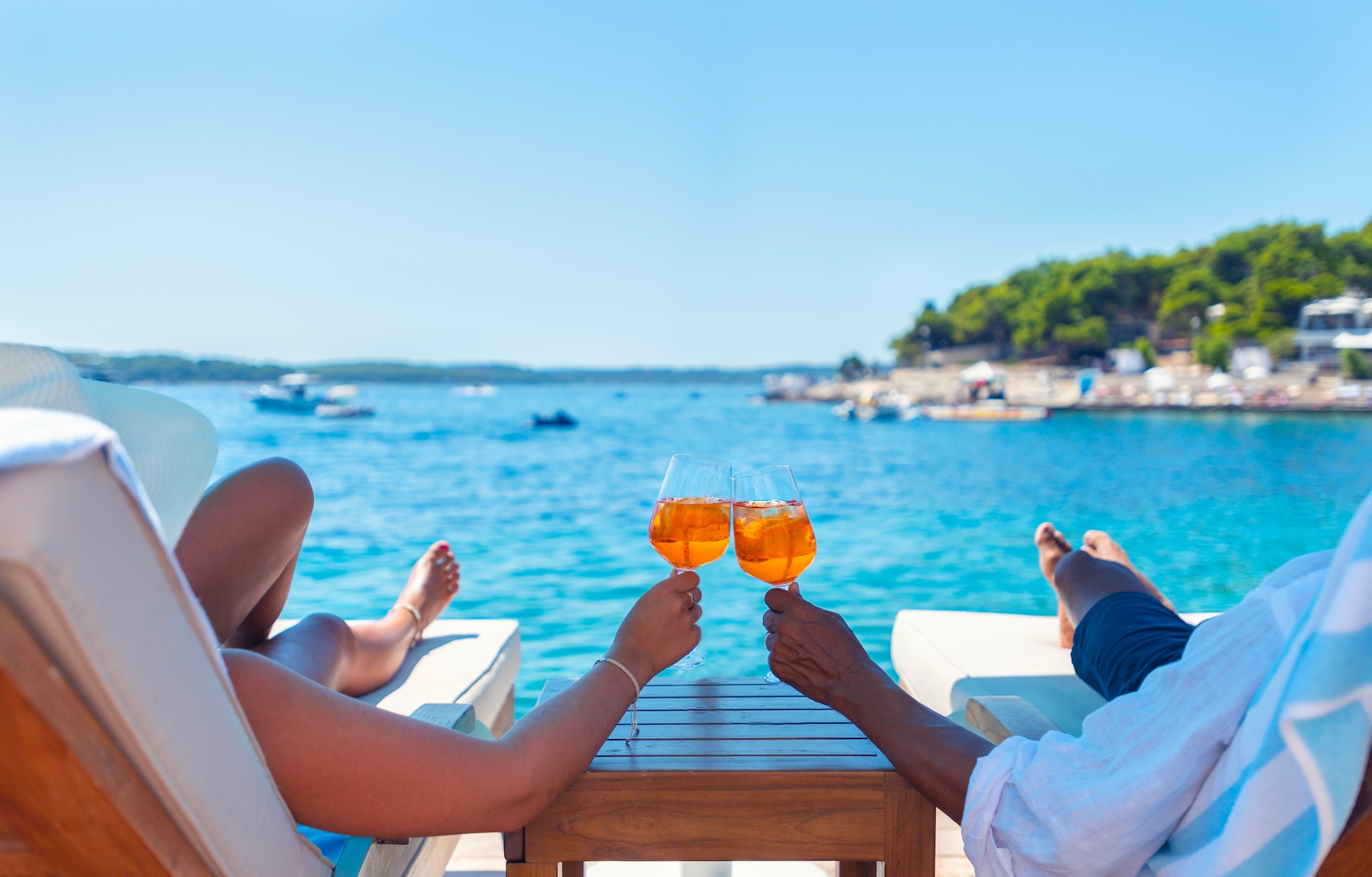 {"metadata_en_GB":{"alt-text":"Couple relaxing and toasting with a Spritz cocktail on a beach deck over the ocean. Turquoise ocean is crystal clear.  horizon in the distance."}}