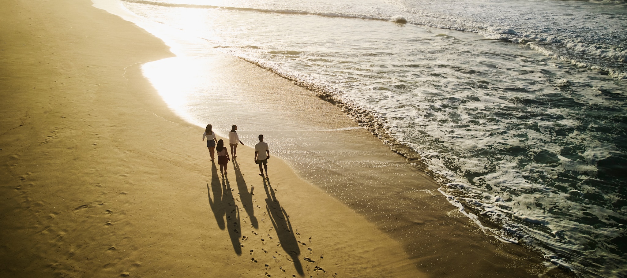 {"metadata_en_GB":{"alt-text":"Wide aerial shot of family walking on tropical beach at sunrise while on vacation"}}