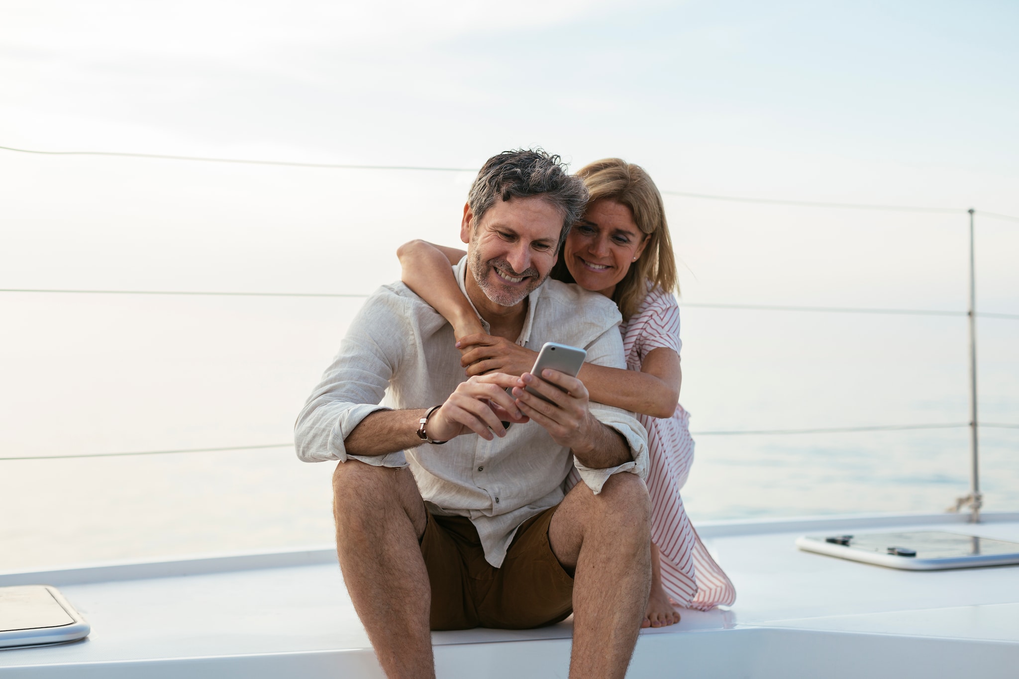 Mature couple looking at smartphone, sitting on a sailing boat