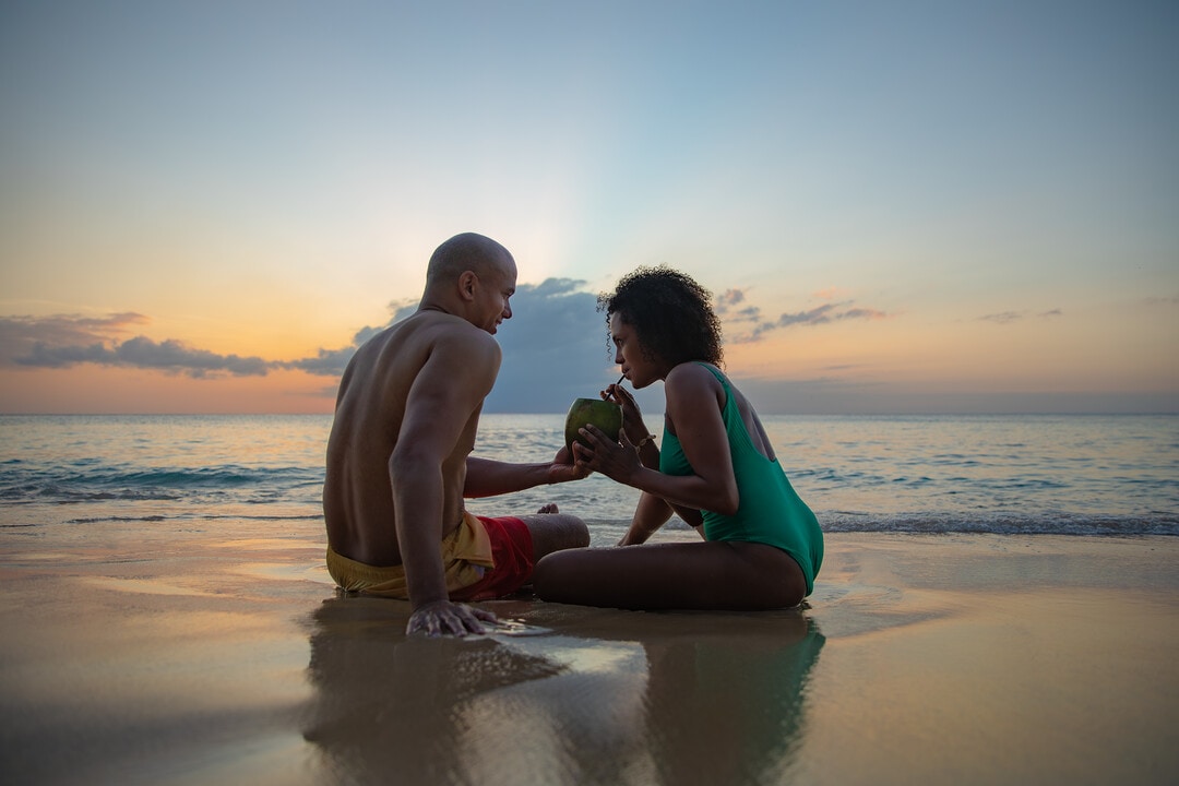 Couple sitting on the beach in Barbados sipping a drink at dusk