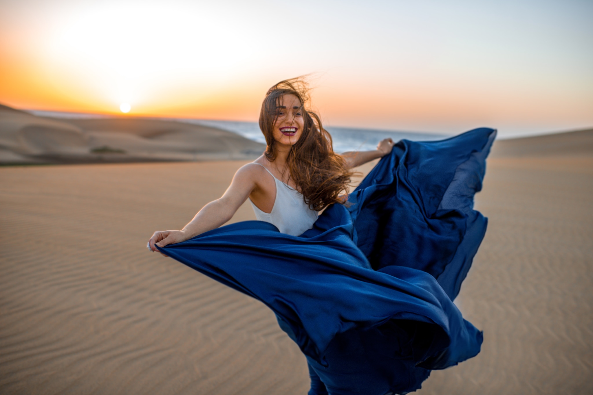 Beautiful young woman with long skirt enjoying the warm wind on the sandy dunes on the sunrise