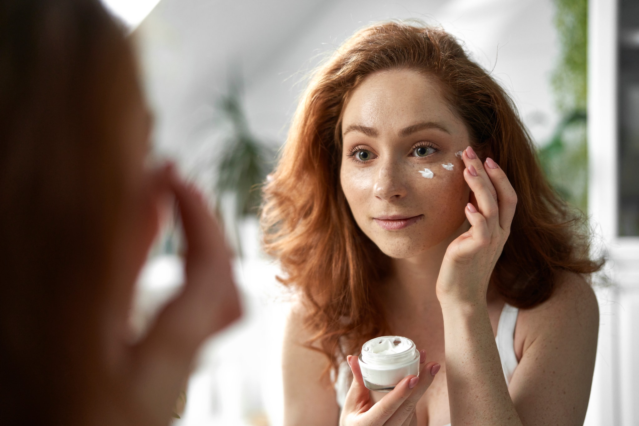 Young caucasian redhead woman smiling and applying face cream