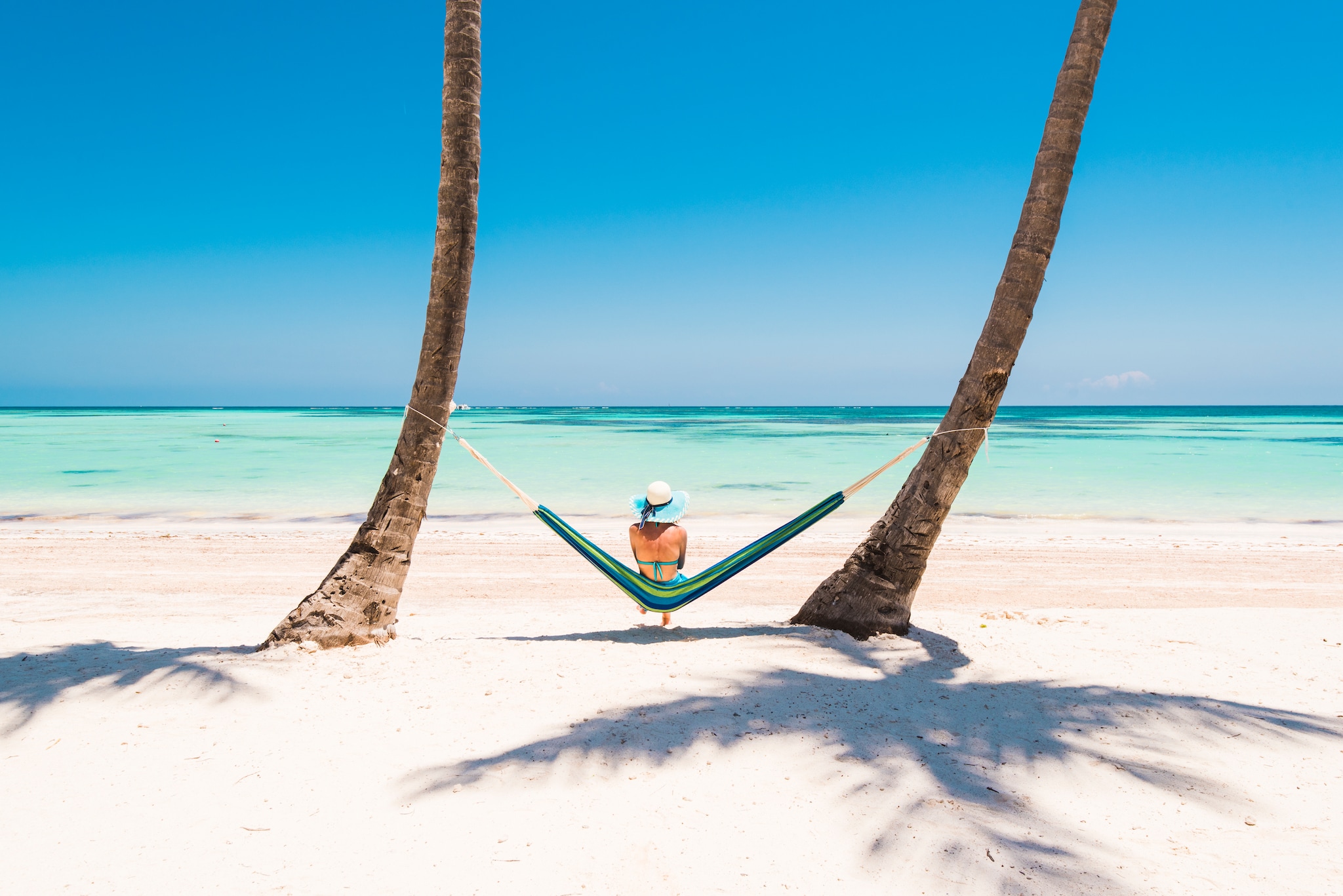 Juanillo Beach (playa Juanillo), Punta Cana, Dominican Republic. Woman relaxing on a hammock on a palm-fringed beach.