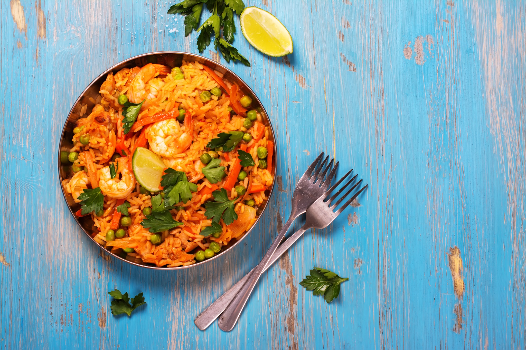 {"metadata_en_GB":{"alt-text":"Traditional spanish paella dish with seafood, peas, rice and chicken over grunge blue background. Top view. Selective focus"}}